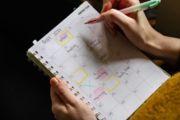 A hand holding a pen, marking dates on a calendar with highlighted boxes.
